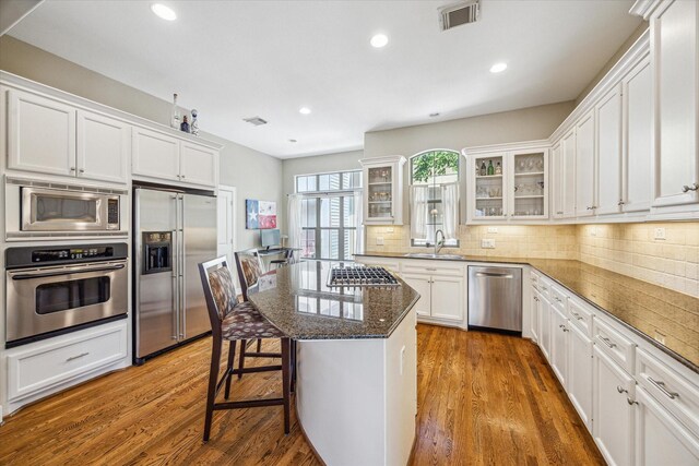 574 Bomar St, Houston, TX 77006 - kitchen with appliances with stainless steel finishes, a sink, white cabinets, wood finished floors, and glass insert cabinets