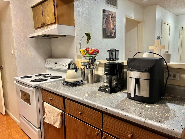12660 Ashford Point Dr Unit 811, Houston, TX 77082 - kitchen featuring electric stove, under cabinet range hood, brown cabinetry, light countertops, and light wood-type flooring