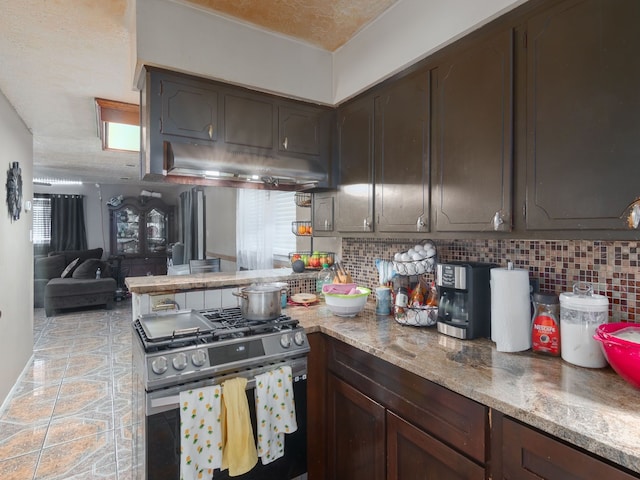 14914 Lawther St, Channelview, TX 77530 - kitchen featuring stainless steel gas stove, decorative backsplash, a peninsula, dark brown cabinets, and under cabinet range hood