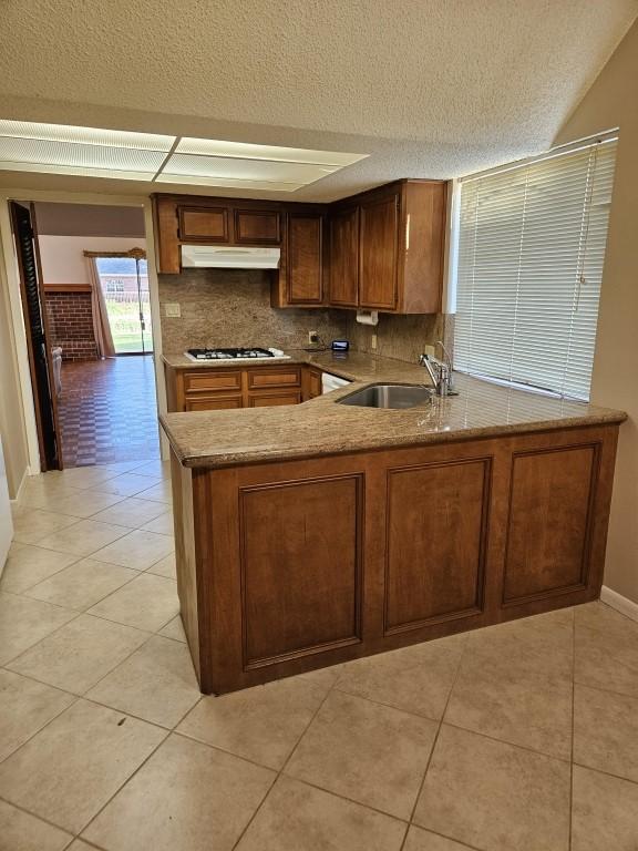19634 Enchanted Oaks Dr, Spring, TX 77388 - kitchen featuring a sink, under cabinet range hood, a textured ceiling, light tile patterned flooring, and white gas stovetop