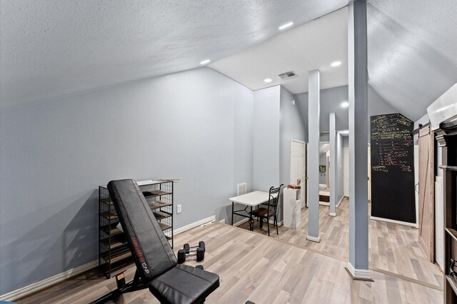 18226 Ennsbury Dr, Houston, TX 77084 - workout room with lofted ceiling, light wood-type flooring, baseboards, a textured ceiling, and a barn door