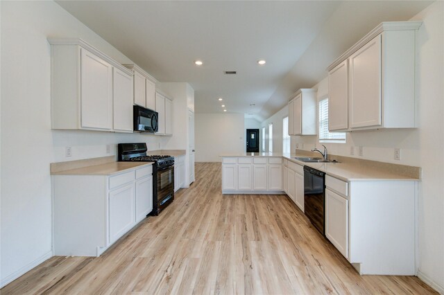 22619 Malvicino Dr, New Caney, TX 77357 - kitchen with black appliances, light wood-style flooring, a sink, a peninsula, and white cabinetry