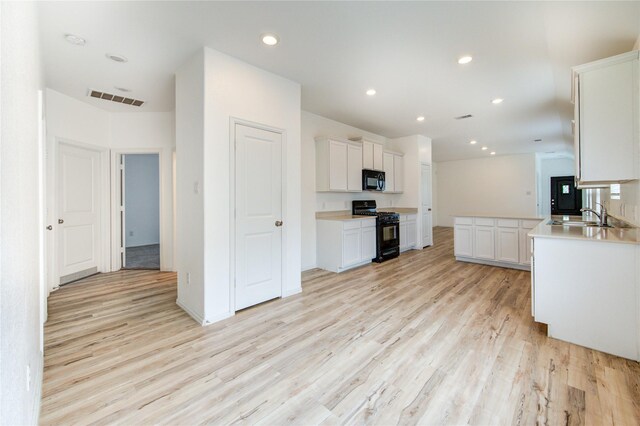 22619 Malvicino Dr, New Caney, TX 77357 - kitchen with black appliances, light wood-style floors, white cabinetry, a sink, and light countertops