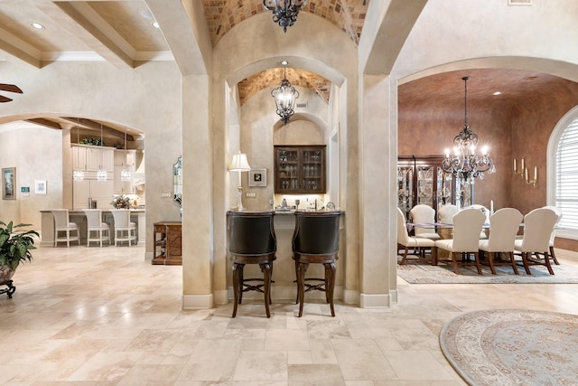 10 Maroon Creek Ct, Spring, TX 77389 - bar area with a chandelier, arched walkways, baseboards, stone tile flooring, and a high ceiling