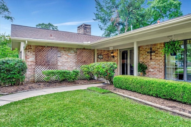 1705 E Texas Ave, Baytown, TX 77520 - view of exterior entry with brick siding, a lawn, and a chimney