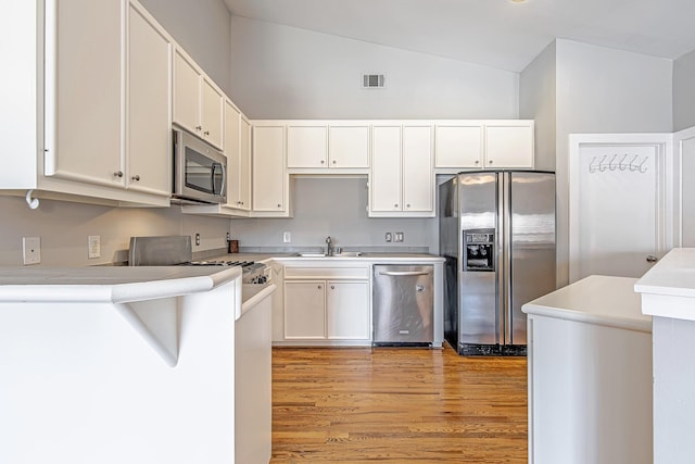 5229 Larkin St, Houston, TX 77007 - kitchen featuring appliances with stainless steel finishes, vaulted ceiling, light wood-style floors, white cabinetry, and light countertops