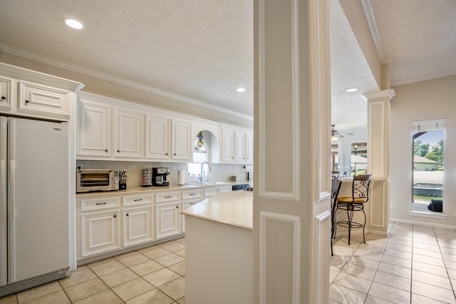13685 Lakeside Place Dr, Willis, TX 77318 - kitchen with freestanding refrigerator, light tile patterned flooring, light countertops, tasteful backsplash, and crown molding