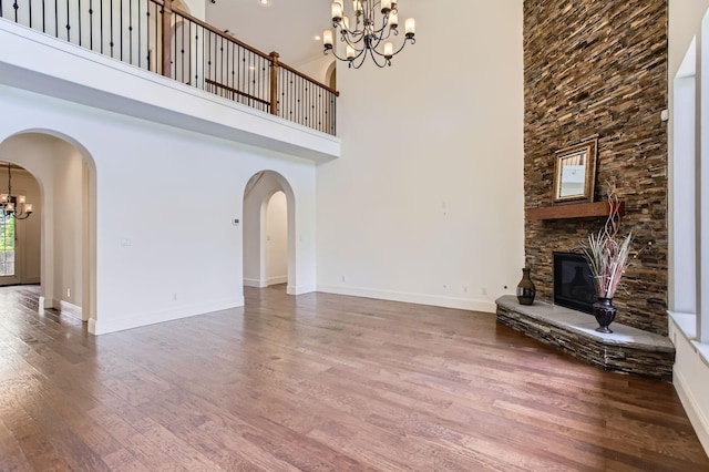 6 Freestone Stream Pl, Spring, TX 77389 - unfurnished living room featuring a chandelier, wood finished floors, a stone fireplace, a towering ceiling, and arched walkways