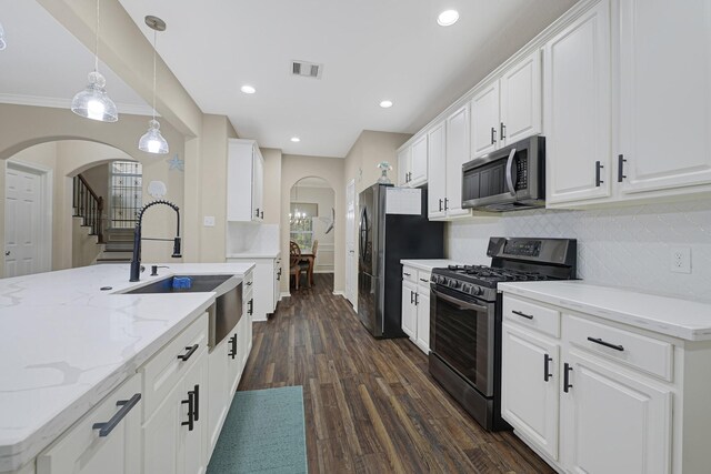 3518 Bain St, Houston, TX 77026 - kitchen with stainless steel appliances, arched walkways, a sink, dark wood finished floors, and white cabinets