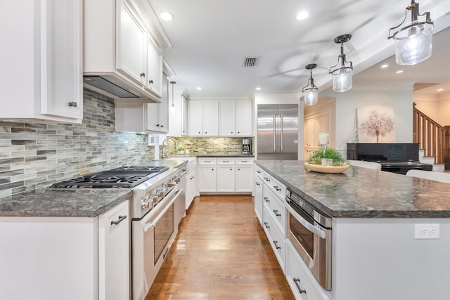 970 W 41st St, Houston, TX 77018 - kitchen with high quality appliances, white cabinetry, decorative backsplash, light wood-style floors, and hanging light fixtures