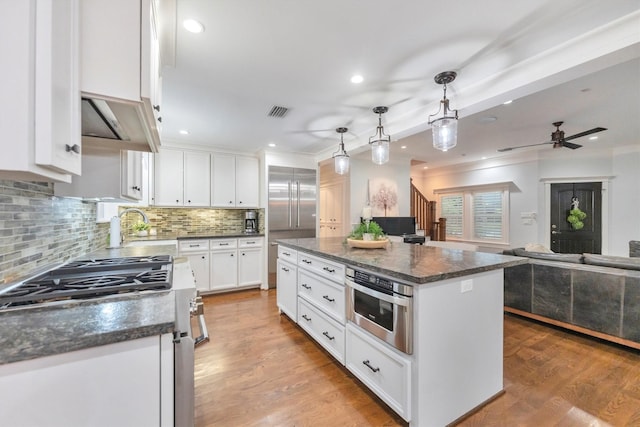 970 W 41st St, Houston, TX 77018 - kitchen with stainless steel appliances, white cabinets, decorative backsplash, range hood, and decorative light fixtures