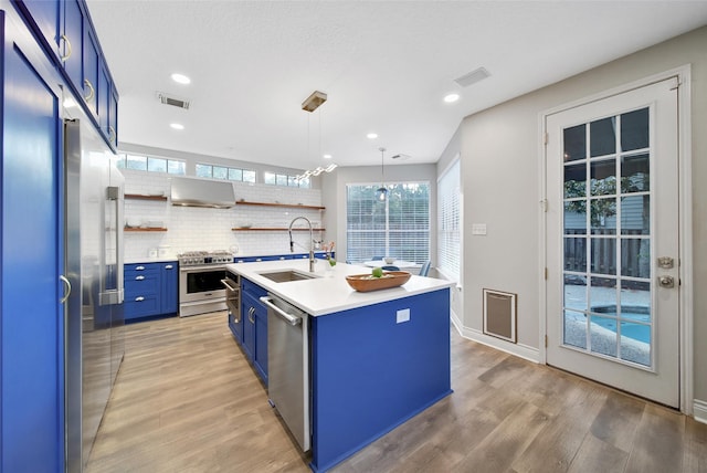 18 Heather Wisp Ct, Spring, TX 77381 - kitchen featuring blue cabinets, appliances with stainless steel finishes, wall chimney exhaust hood, a sink, and open shelves