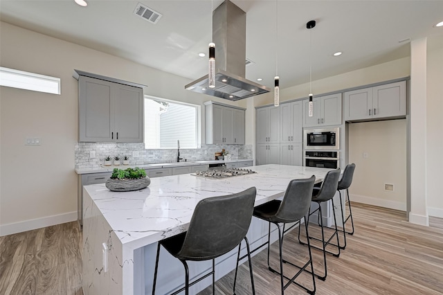 2905 Nagle St, Houston, TX 77004 - kitchen featuring stainless steel appliances, gray cabinets, island range hood, a spacious island, and light stone countertops