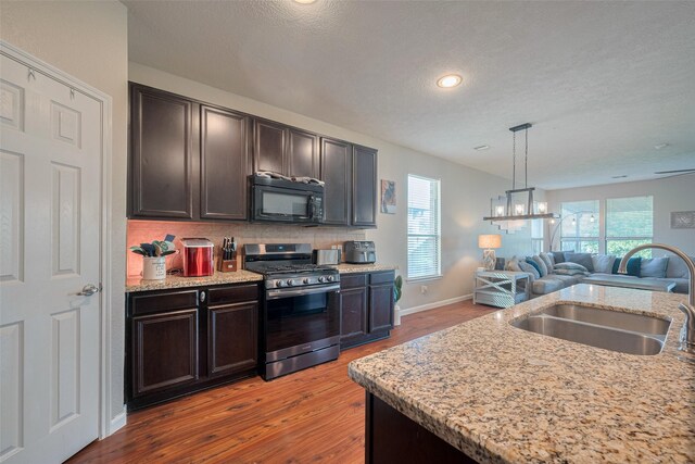 4323 N Vineyard Mdw Ln, Katy, TX 77449 - kitchen featuring black microwave, stainless steel gas stove, a sink, open floor plan, and wood finished floors