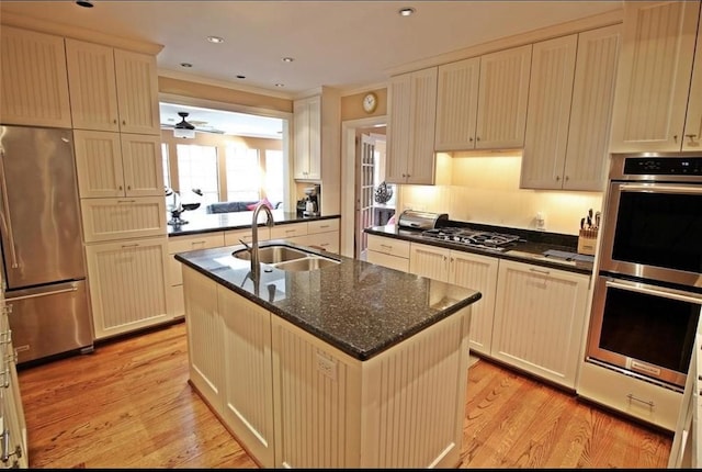 1216 S Shepherd Dr, Houston, TX 77019 - kitchen with appliances with stainless steel finishes, a sink, light wood finished floors, a center island with sink, and dark stone countertops