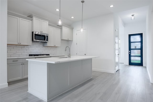 829 Laguna Green Ln, Katy, TX 77493 - kitchen with stainless steel microwave, a sink, decorative backsplash, light wood finished floors, and a center island with sink