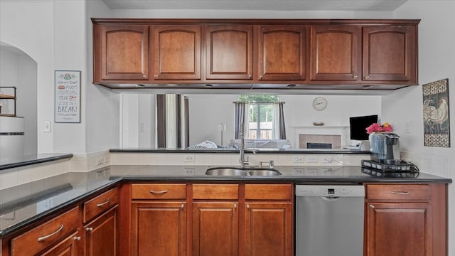 19603 Pitchstone Dr, Tomball, TX 77377 - kitchen with stainless steel dishwasher, a sink, dark stone counters, a tile fireplace, and arched walkways