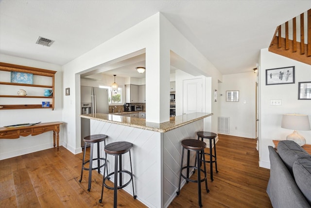 3411 Petite Cir, Galveston, TX 77554 - kitchen featuring stainless steel refrigerator with ice dispenser, dark wood-style flooring, a breakfast bar, and light stone countertops