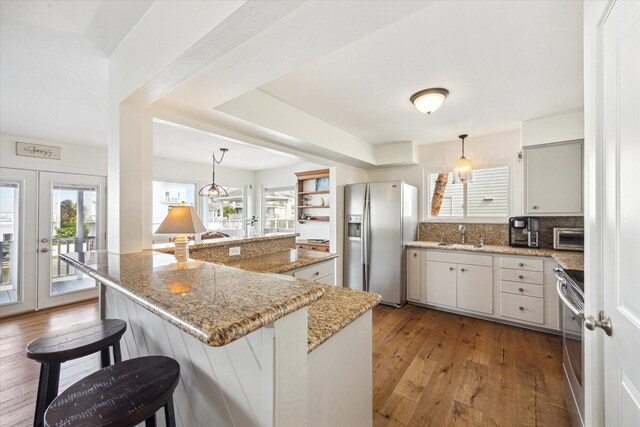 3411 Petite Cir, Galveston, TX 77554 - kitchen featuring stainless steel refrigerator with ice dispenser, stove, hardwood / wood-style floors, a breakfast bar area, and decorative light fixtures