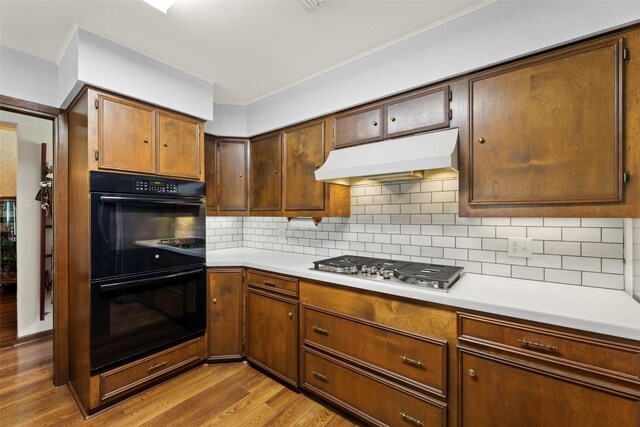 613 Bolling Green Dr, Wharton, TX 77488 - kitchen with under cabinet range hood, light wood-style flooring, stainless steel gas stovetop, light countertops, and tasteful backsplash