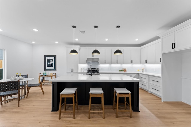 514 Melbourne St Unit B, Houston, TX 77022 - kitchen with stove, under cabinet range hood, backsplash, a kitchen island with sink, and light countertops