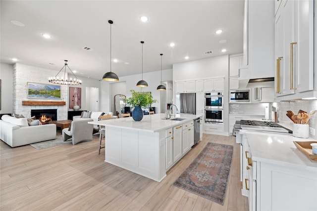 7851 Longhorn Trl, Fulshear, TX 77406 - kitchen with stainless steel appliances, white cabinetry, a fireplace, open floor plan, and decorative backsplash