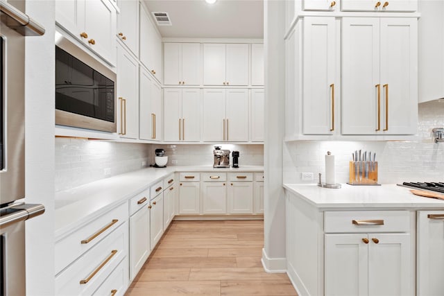 7851 Longhorn Trl, Fulshear, TX 77406 - kitchen with stainless steel microwave, white cabinetry, light wood-type flooring, light countertops, and decorative backsplash