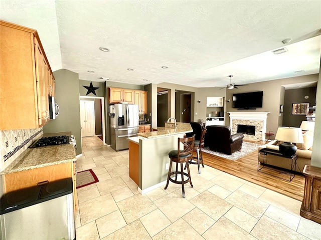 8910 Everhart Ln, Houston, TX 77040 - kitchen with stainless steel appliances, a ceiling fan, a breakfast bar area, a stone fireplace, and open floor plan