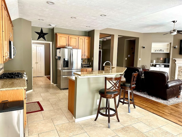 8910 Everhart Ln, Houston, TX 77040 - kitchen with appliances with stainless steel finishes, a kitchen breakfast bar, open floor plan, ceiling fan, and light stone countertops
