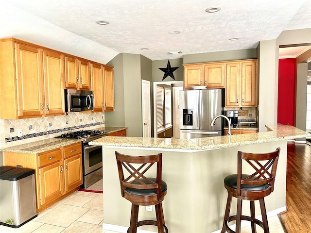 8910 Everhart Ln, Houston, TX 77040 - kitchen featuring appliances with stainless steel finishes, a breakfast bar, backsplash, light stone countertops, and a textured ceiling