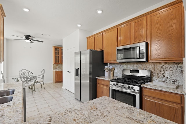 6426 Savannah Pines Dr, Katy, TX 77449 - kitchen featuring stainless steel appliances, ceiling fan, light tile patterned flooring, decorative backsplash, and brown cabinetry