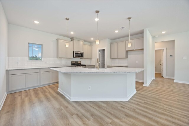 540 Barton Place Dr, Cleveland, TX 77327 - kitchen featuring stainless steel appliances, a sink, tasteful backsplash, an island with sink, and light wood finished floors