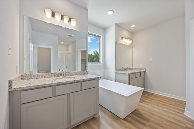 540 Barton Place Dr, Cleveland, TX 77327 - bathroom featuring a shower stall, a freestanding tub, wood finished floors, two vanities, and baseboards