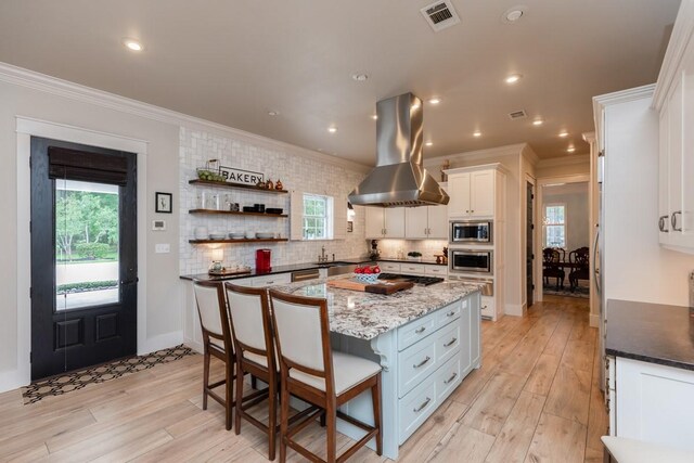 5950 Keith Rd, Lumberton, TX 77657 - kitchen featuring island range hood, ornamental molding, stainless steel microwave, white cabinetry, and light wood-type flooring