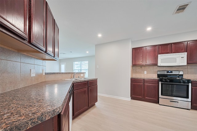 1219 Newsome Glenn Dr, Houston, TX 77090 - kitchen with white microwave, stainless steel gas range, light wood finished floors, decorative backsplash, and recessed lighting