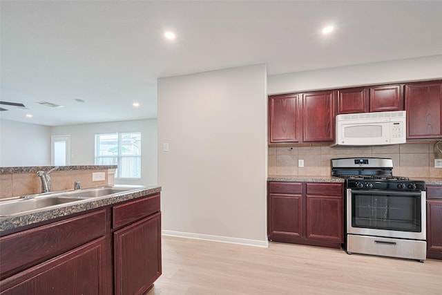 1219 Newsome Glenn Dr, Houston, TX 77090 - kitchen with white microwave, stainless steel range with gas stovetop, a sink, decorative backsplash, and light wood-style flooring