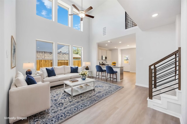 16846 Needlepoint Dr, Conroe, TX 77302 - living room with stairs, light wood-type flooring, a ceiling fan, a towering ceiling, and baseboards