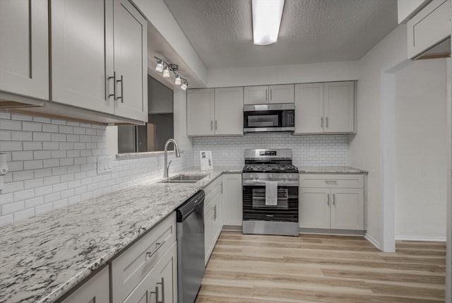 1041 Crossing Rd, Angleton, TX 77515 - kitchen featuring appliances with stainless steel finishes, light wood-style flooring, a textured ceiling, light stone counters, and backsplash