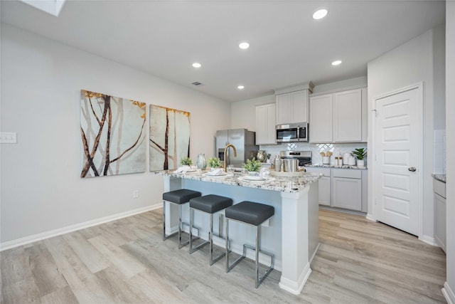 11745 Whirlaway Dr, Willis, TX 77318 - kitchen with stainless steel appliances, light wood-style floors, a breakfast bar area, a center island with sink, and light stone counters