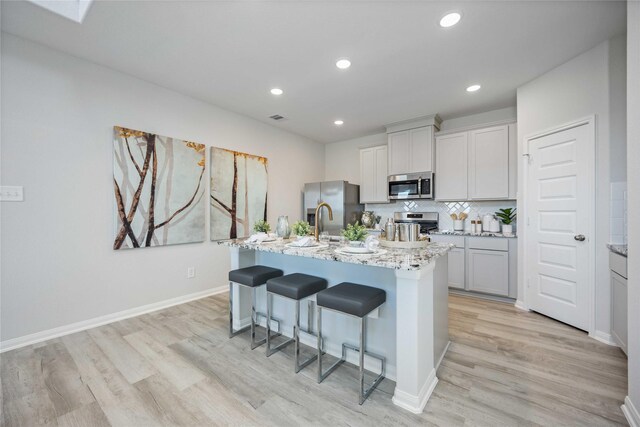 506 Tejas Village Pkwy, Beasley, TX 77417 - kitchen with stainless steel appliances, light wood-style floors, a breakfast bar area, a center island with sink, and light stone counters