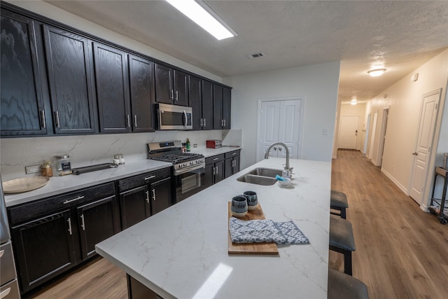 3017 Cambridge Meadows Ln, Dickinson, TX 77539 - kitchen with appliances with stainless steel finishes, a sink, a kitchen breakfast bar, light wood-style floors, and dark cabinets