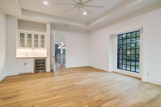 830 Azalea St, Houston, TX 77018 - empty room featuring beverage cooler, bar with sink, a tray ceiling, light wood-style floors, and a ceiling fan
