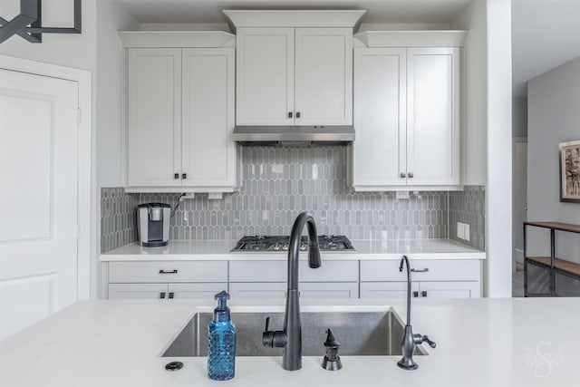 5106 Green Leaf Ln, Fulshear, TX 77441 - kitchen with under cabinet range hood, stainless steel gas cooktop, light countertops, backsplash, and white cabinetry
