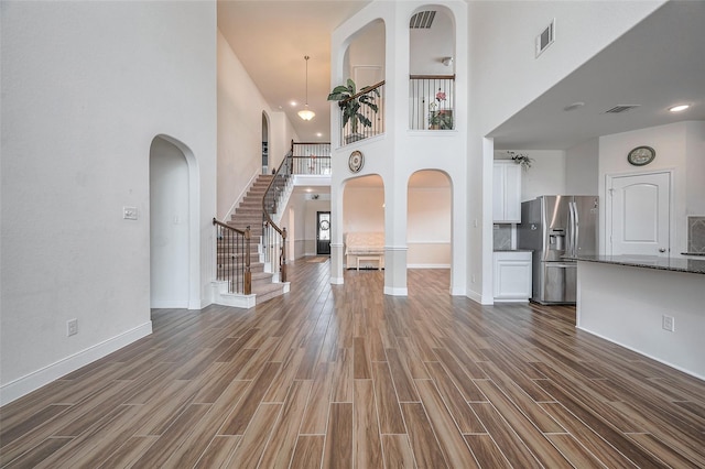 11202 Bluewater Lagoon Cir, Cypress, TX 77433 - unfurnished living room featuring a high ceiling, dark wood-type flooring, baseboards, stairway, and arched walkways
