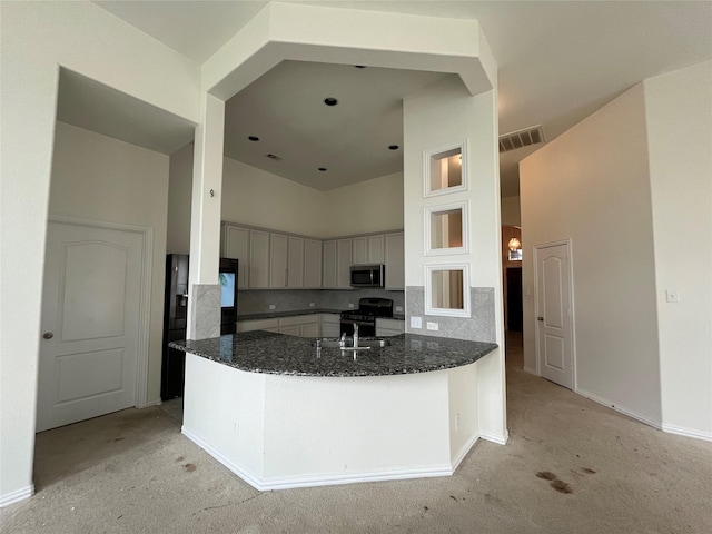31909 Mckinley Run Dr, Hockley, TX 77447 - kitchen with appliances with stainless steel finishes, a towering ceiling, dark stone countertops, light colored carpet, and a peninsula