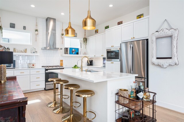 1747 Ojeman Spring Ln, Houston, TX 77055 - kitchen featuring wall chimney range hood, stainless steel appliances, light wood-type flooring, a breakfast bar area, and recessed lighting