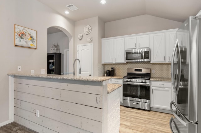 1724 Wandering Hills Rd, Conroe, TX 77304 - kitchen featuring appliances with stainless steel finishes, light stone counters, light wood-style floors, arched walkways, and vaulted ceiling