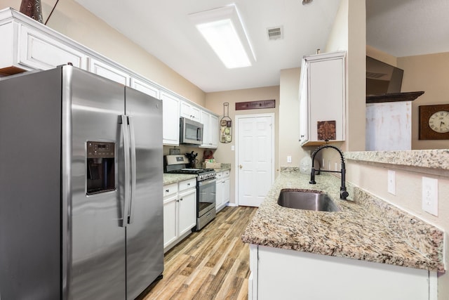 259 Adobe Ter S, Conroe, TX 77316 - kitchen with stainless steel appliances, a sink, light wood finished floors, white cabinetry, and light stone countertops