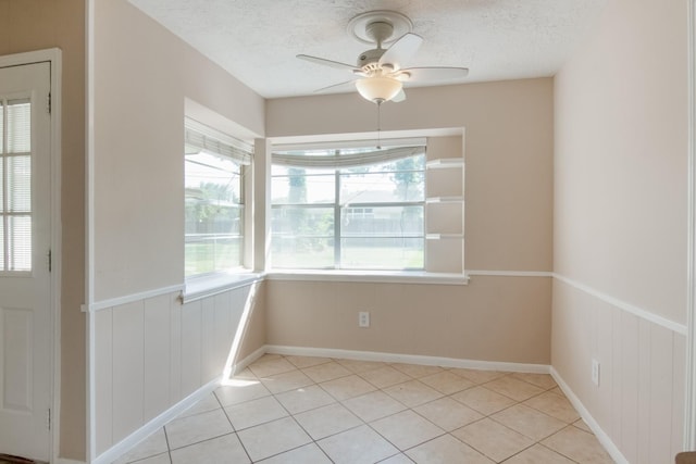 12503 Tall Forest Dr, Cypress, TX 77429 - unfurnished dining area featuring a textured ceiling, ceiling fan, light tile patterned floors, and a wainscoted wall