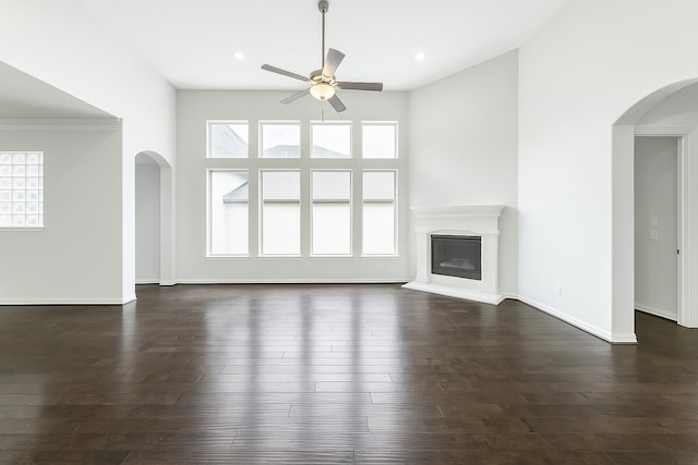 11 Floral Hills Ln, Fulshear, TX 77441 - unfurnished living room featuring a ceiling fan, arched walkways, a glass covered fireplace, dark wood-style flooring, and recessed lighting